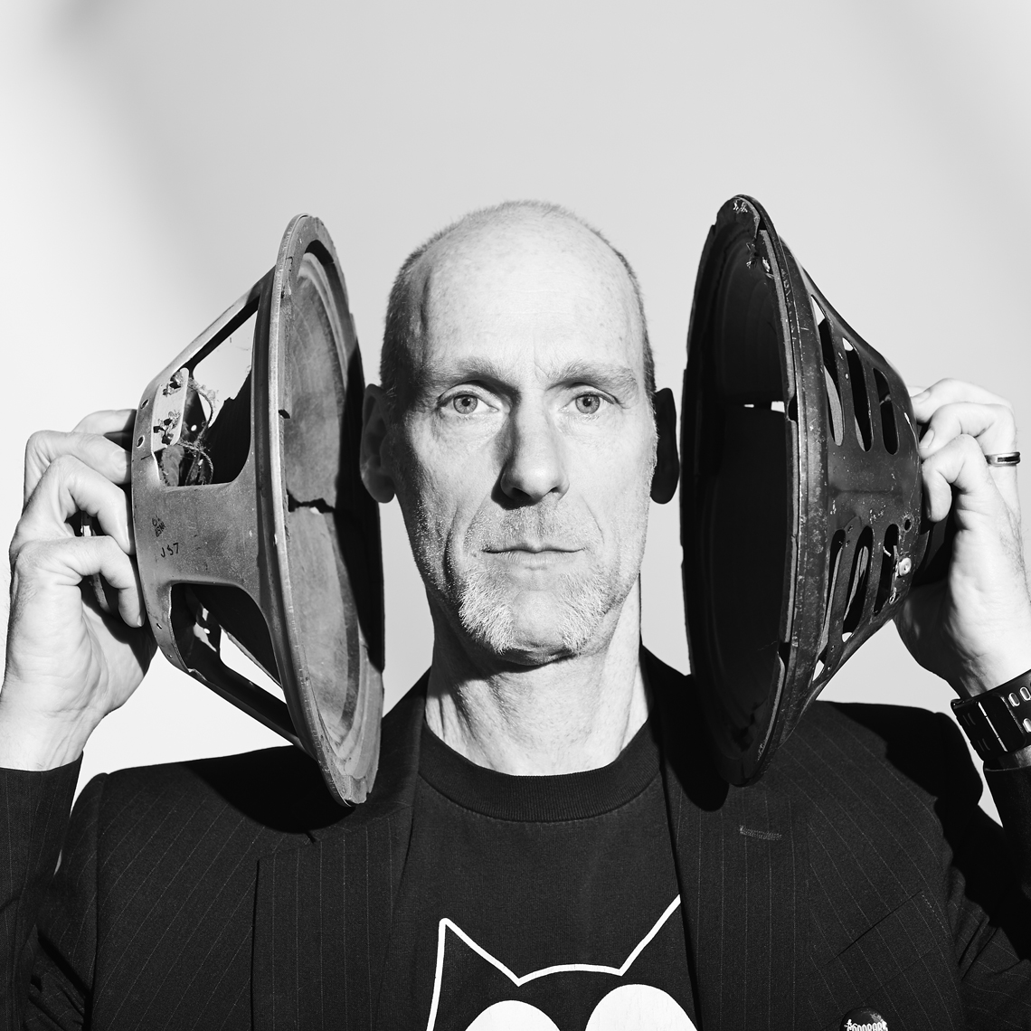 Black and White portrait of bald white man holding speakers over his ears