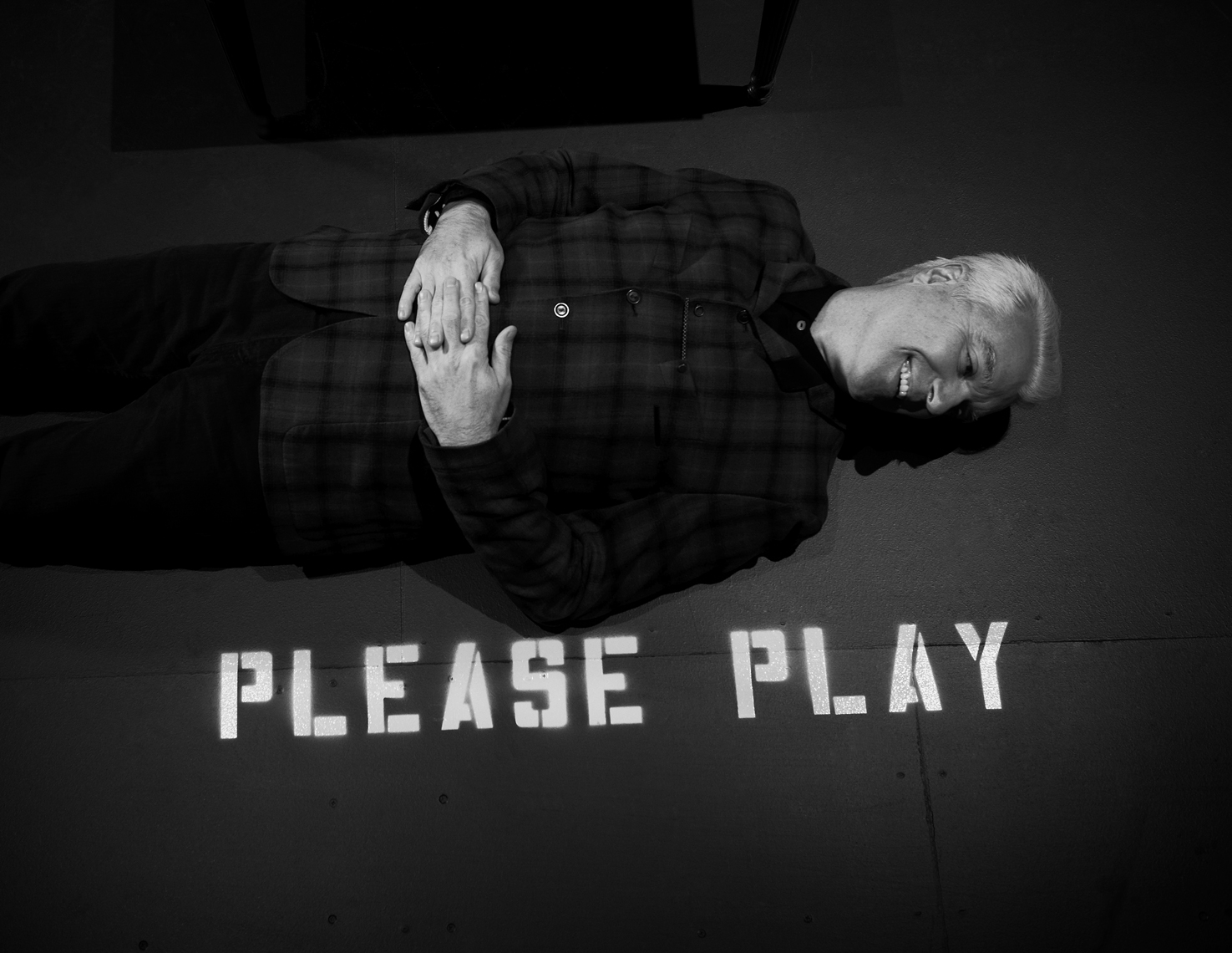 David Byrne laying on the floor with the words Please Play