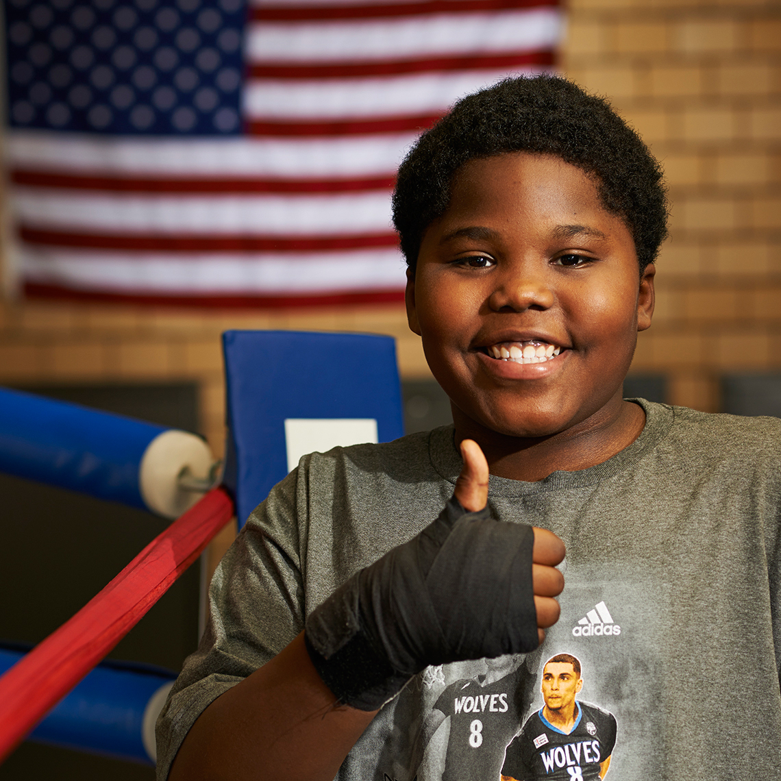 Heavyset kid with thumbs up in boxing ring